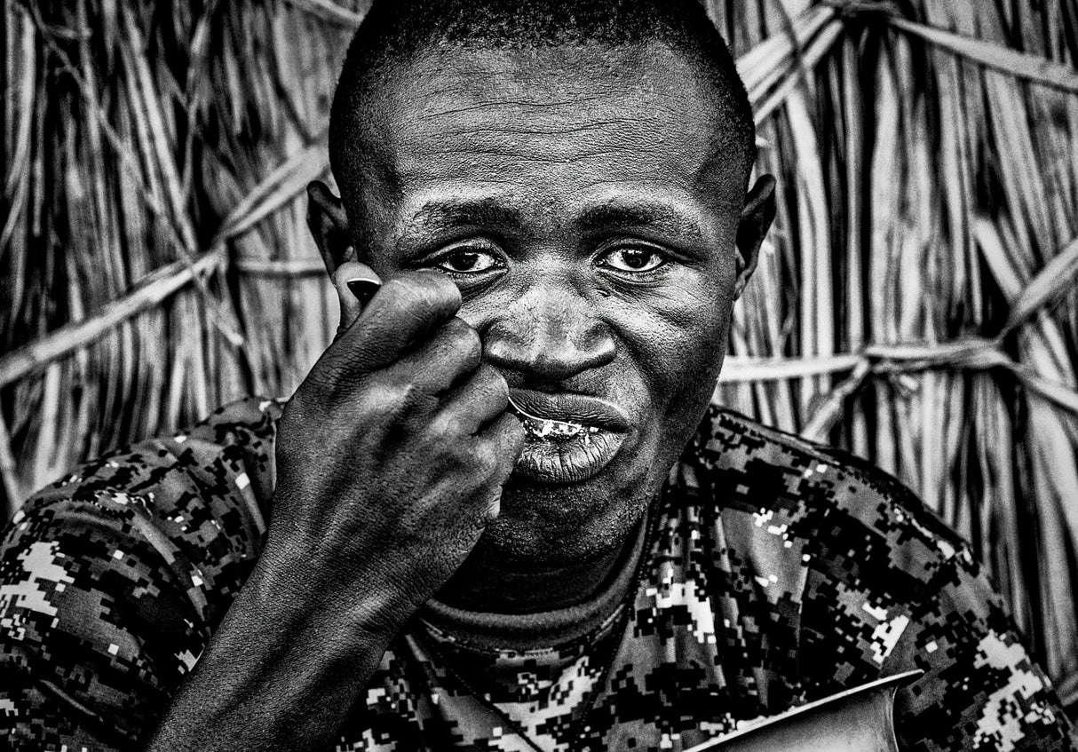 El Molo ethnic man eating at the entrance of his home. Poster och Canvastavla