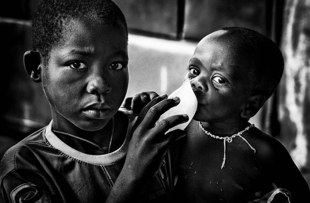 Quenching his brother´s thirst with a frozen water bag - Benin Poster och Canvastavla