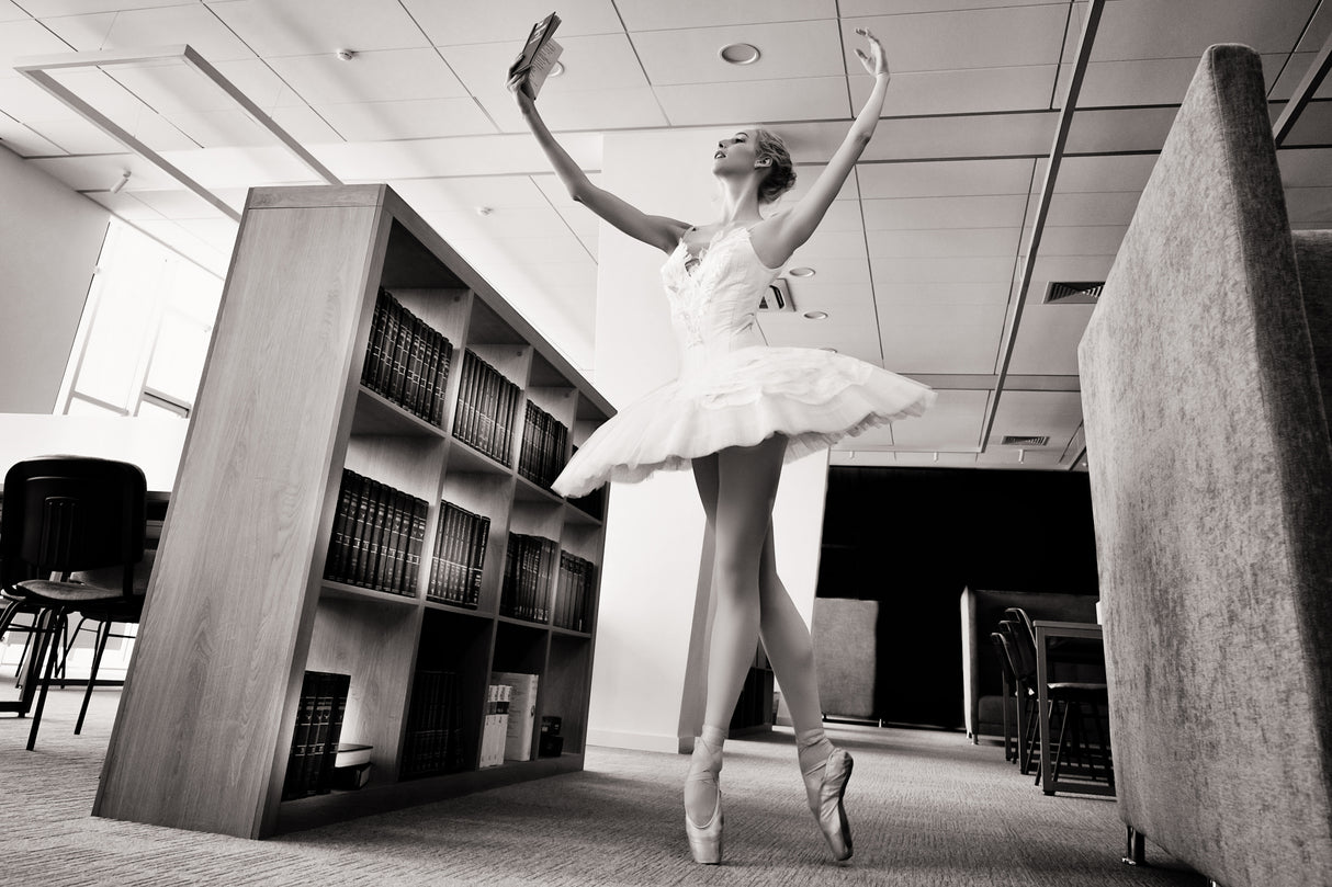 the Dreamer. ballerina on pointe shoes in the library reads a book holding it up Poster och Canvastavla