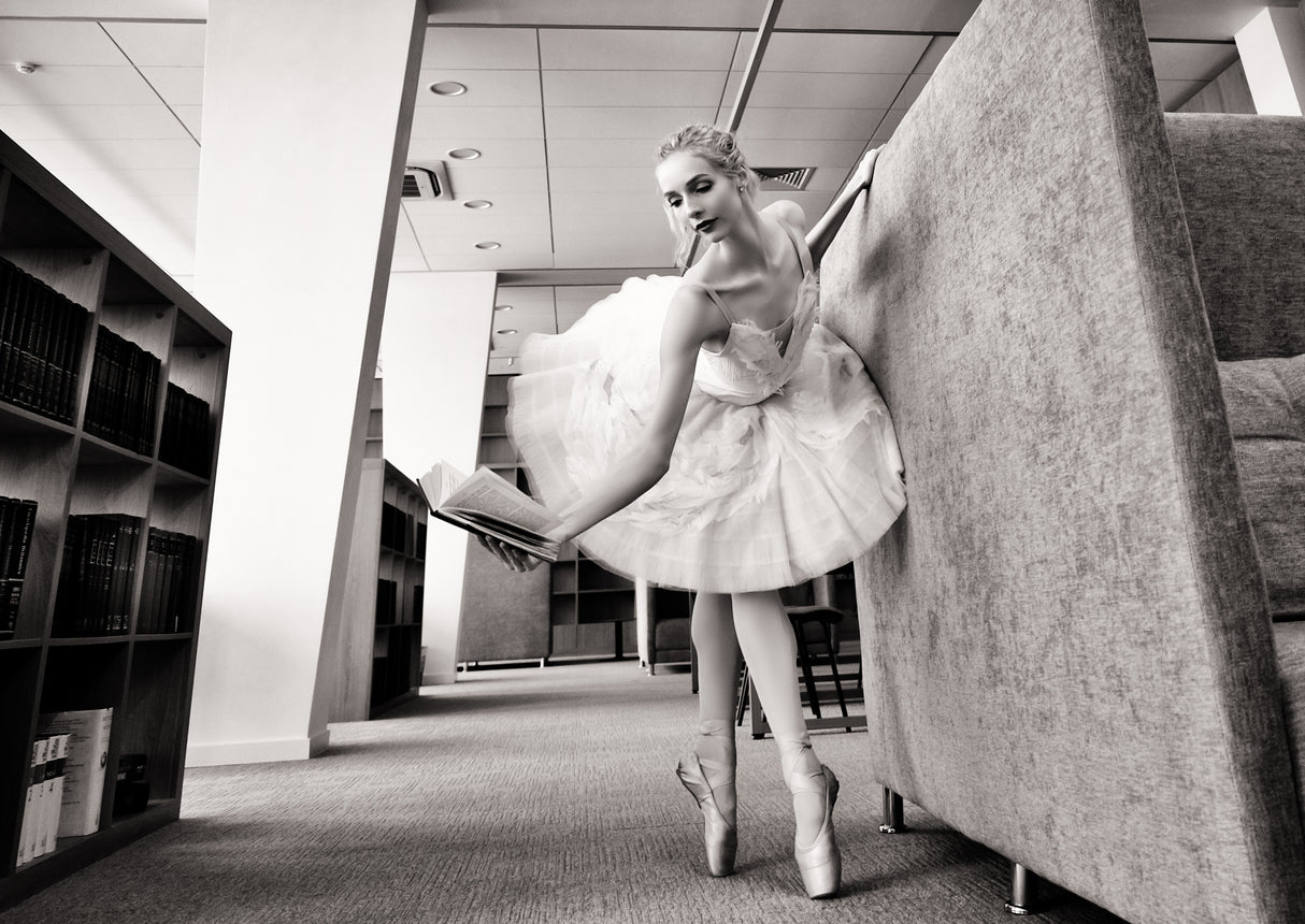 ballerina on pointe shoes in the library reads a book holding it up Poster och Canvastavla