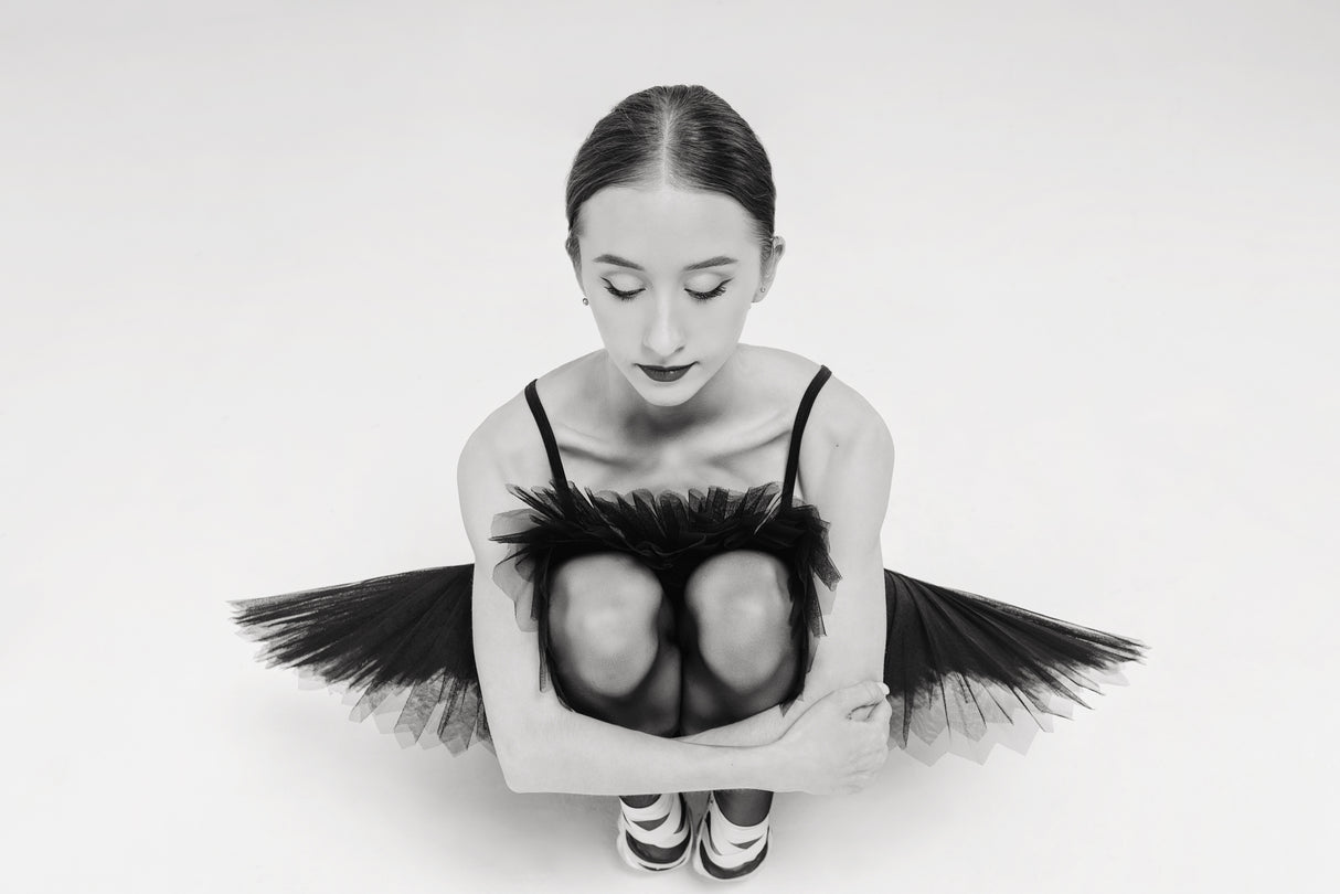 a portrait of a ballerina in a black tutu squatting hugging her knees Poster och Canvastavla